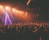 Escenario de concierto con iluminación envolvente y multitud emocionada durante actuación en directo