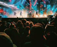 Escenario de concierto pop con luces intensas y público en un gran recinto