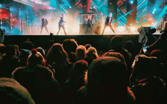 Escenario de concierto pop con luces intensas y público en un gran recinto