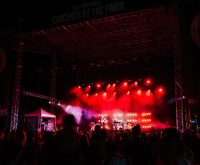 Ambiente de festival de música al aire libre con público y escenario iluminado en día de verano