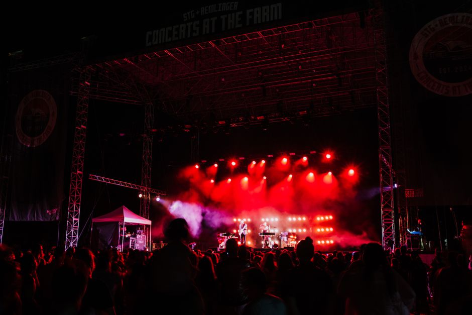 Ambiente de festival de música al aire libre con público y escenario iluminado en día de verano