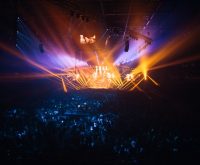 Ambiente de concierto nocturno con luces de escenario y público expectante
