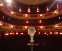 Escenario de concierto pop con foco solitario y micrófono, evocando pausa y reflexión