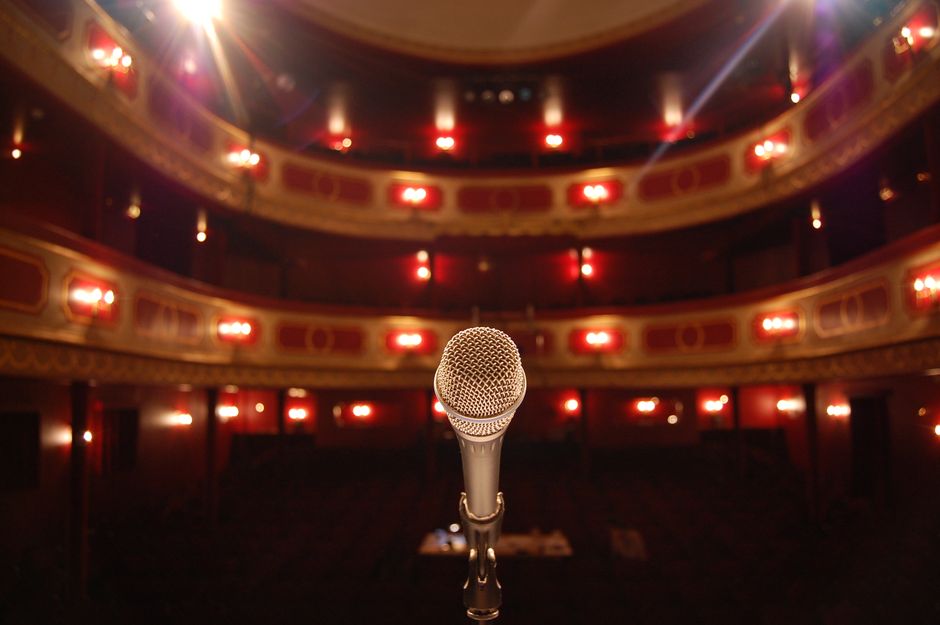 Escenario de concierto pop con foco solitario y micrófono, evocando pausa y reflexión