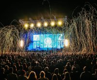 Escenario de festival con iluminación intensa y multitud durante un concierto de metal alternativo