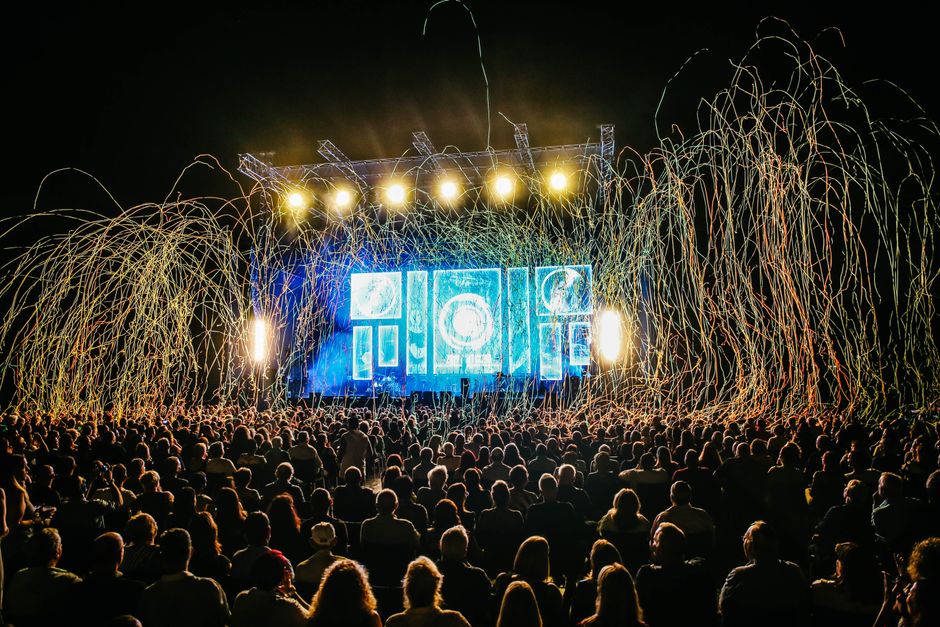 Escenario de festival con iluminación intensa y multitud durante un concierto de metal alternativo