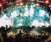 Escenario de festival de música independiente con público y luces al anochecer