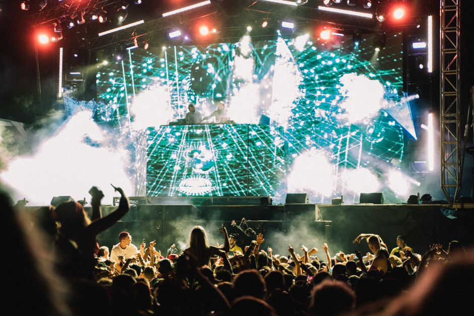 Escenario de festival de música independiente con público y luces al anochecer