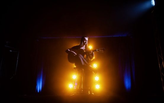 Imagen ilustrativa. Atmósfera de concierto de rumba con guitarra española y luces de escenario.