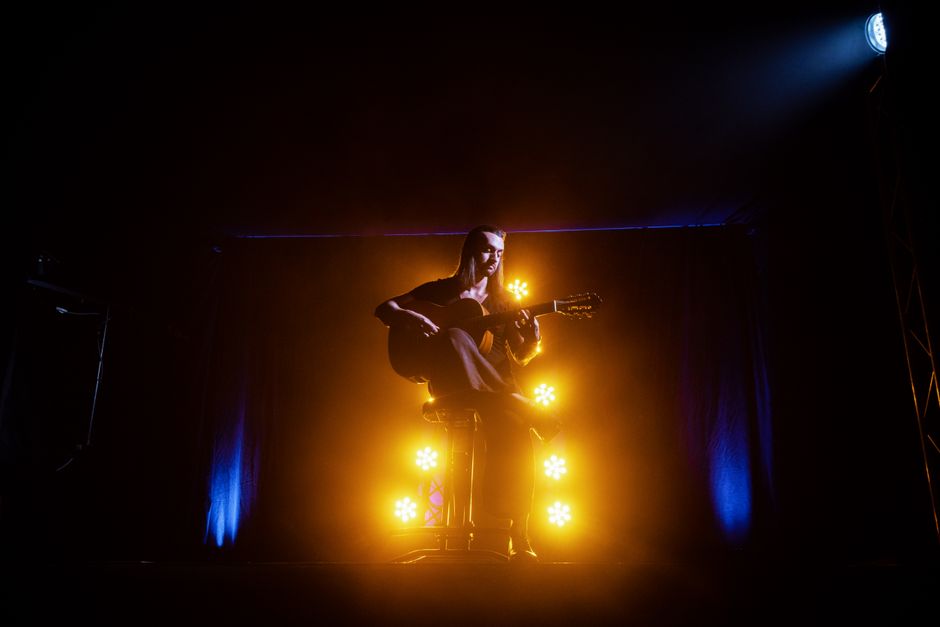 Imagen ilustrativa. Atmósfera de concierto de rumba con guitarra española y luces de escenario.